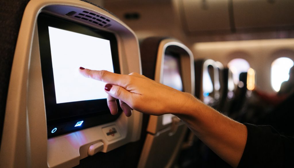 A female hand touches a seat back screen onboard a plane