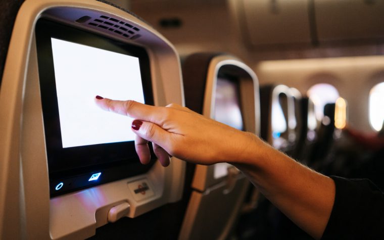 A female hand touches a seat back screen onboard a plane