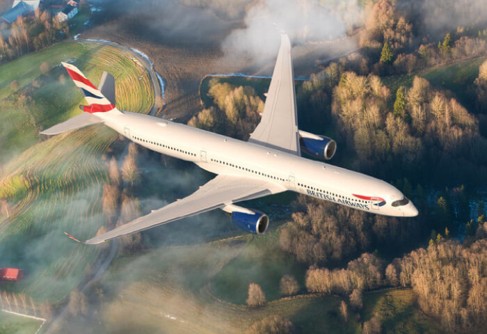 A British Airways plane flying with forest and farm land below it.