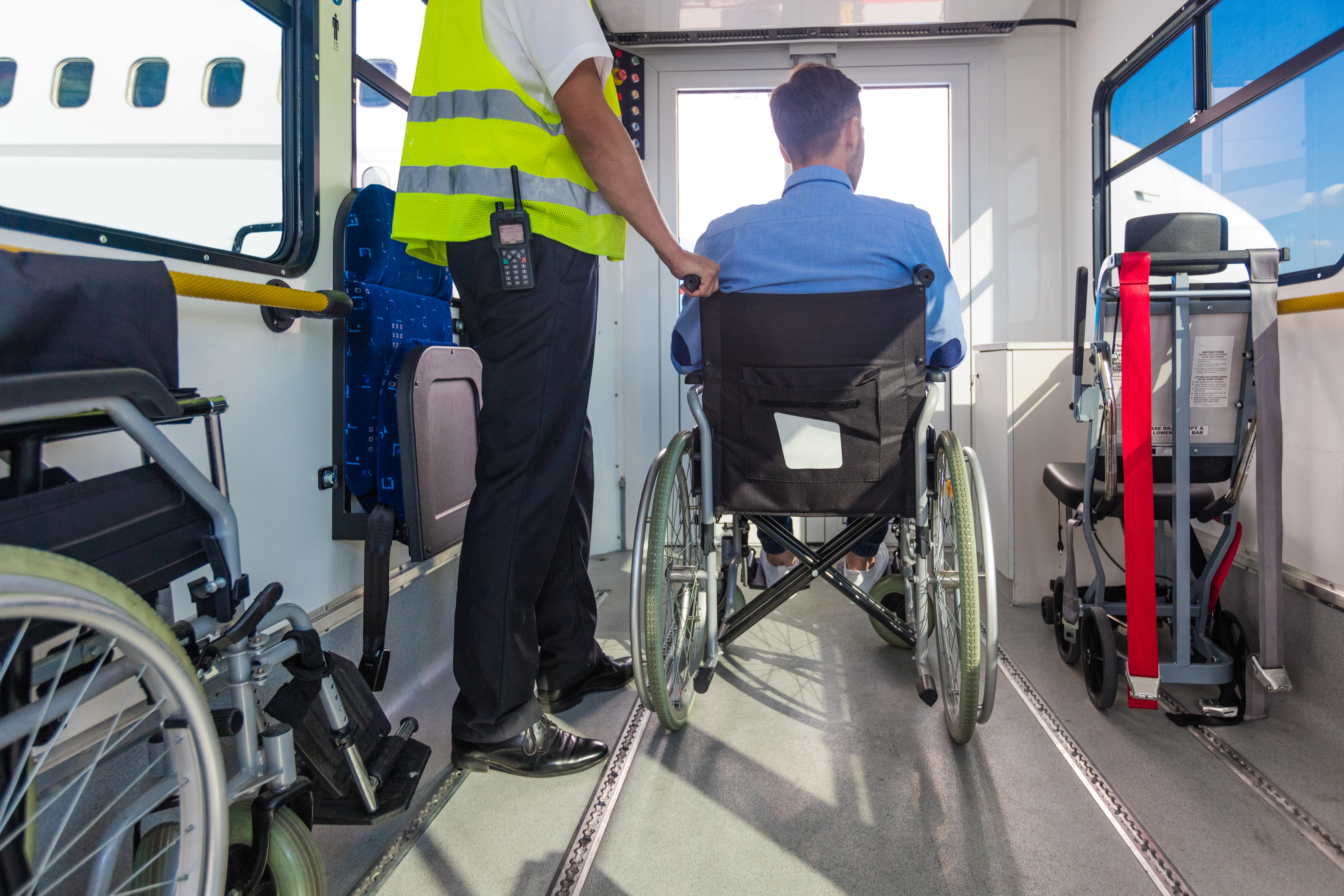 Service man helping disabled passenger to enter on board at airport from behind