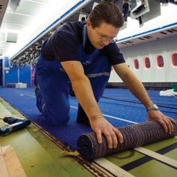 man rolling carpet onto floor of airplane interior