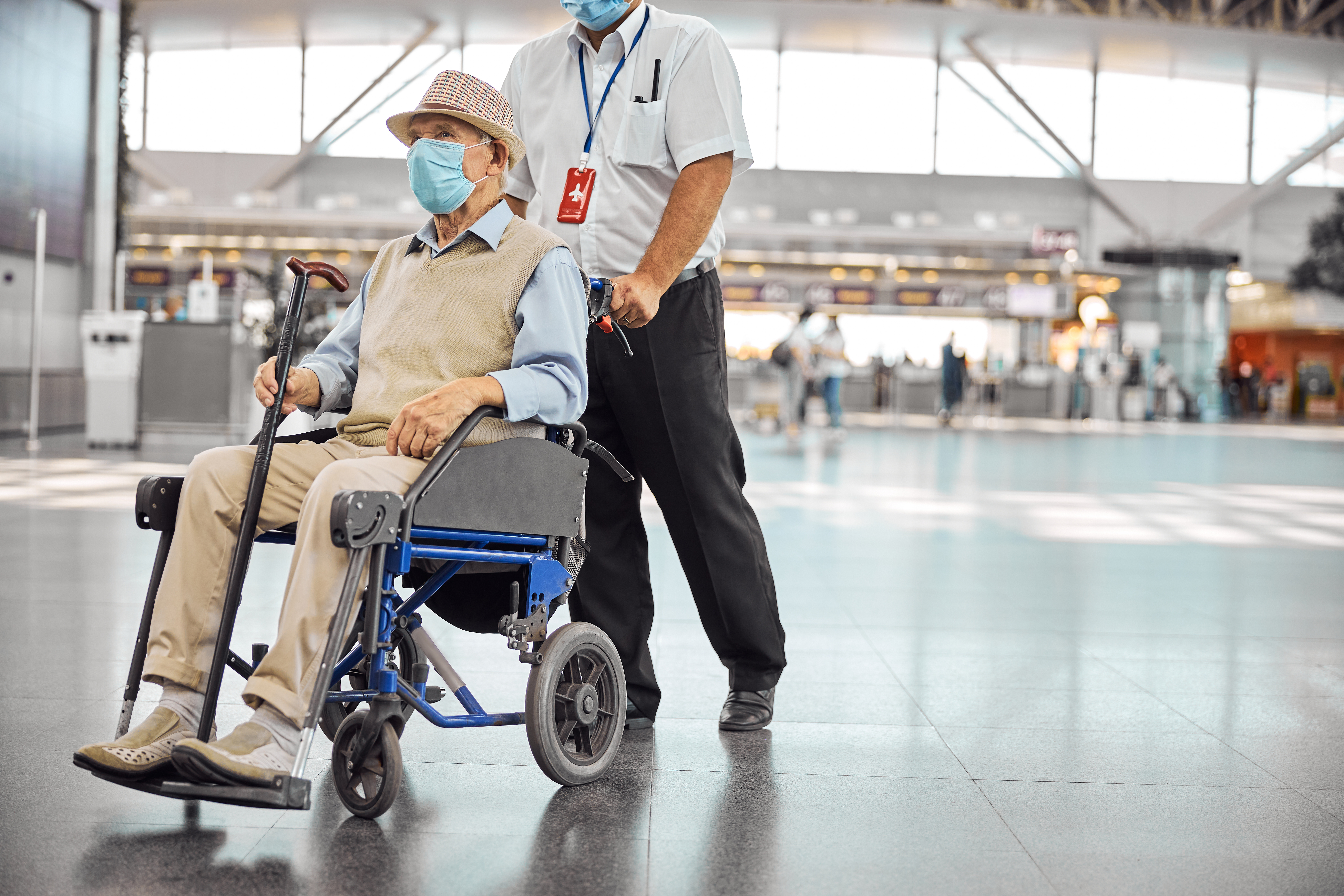 Serious aged Caucasian male tourist in a disposable protective mask sitting in a transport chair
